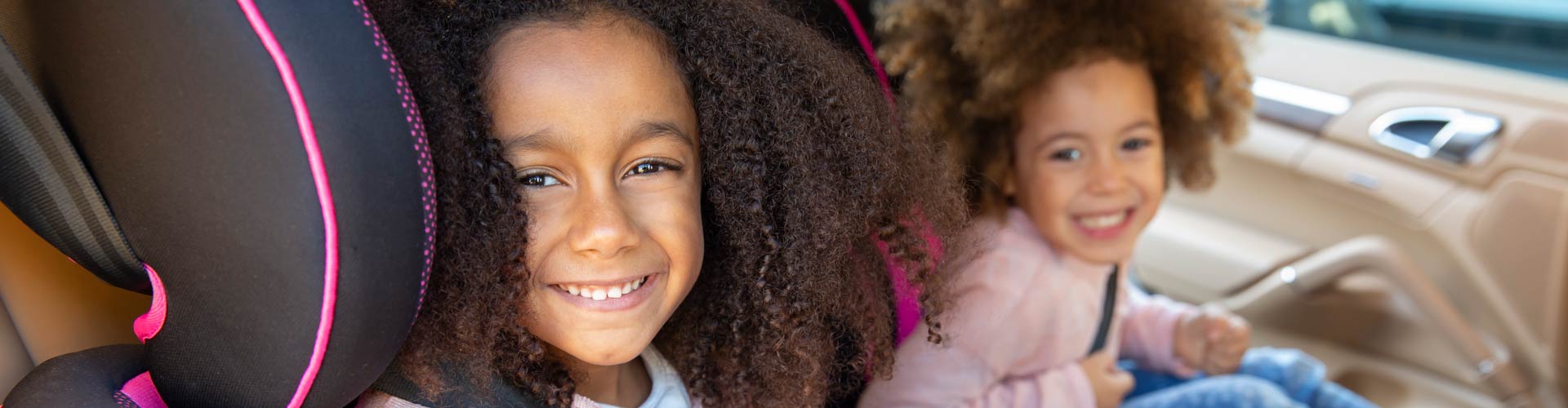 Two smiling girls in child seats in back of car