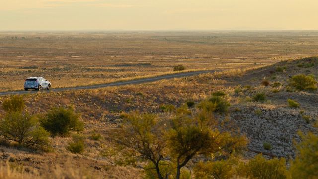 An electric vehicle drives across the outback at dusk