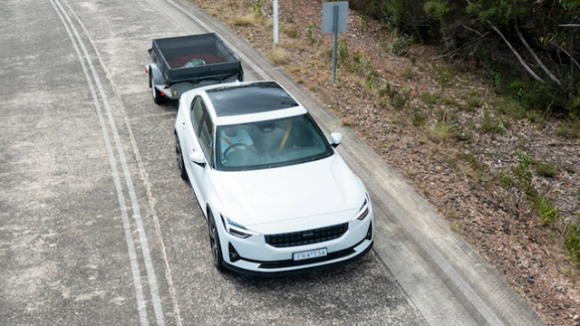 A white electric vehicle towing a small trailer along a road in the country.