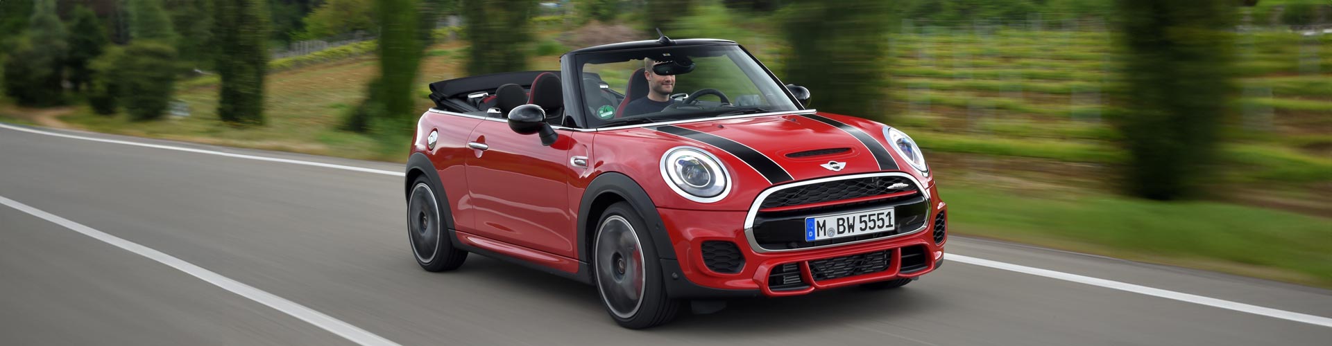 A red Mini convertible speeds along a country road