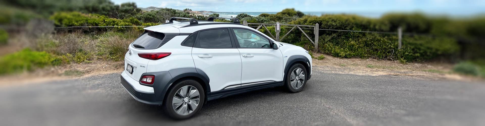 White 2021 Hyundai Kona Electric Highlander in carpark near beach