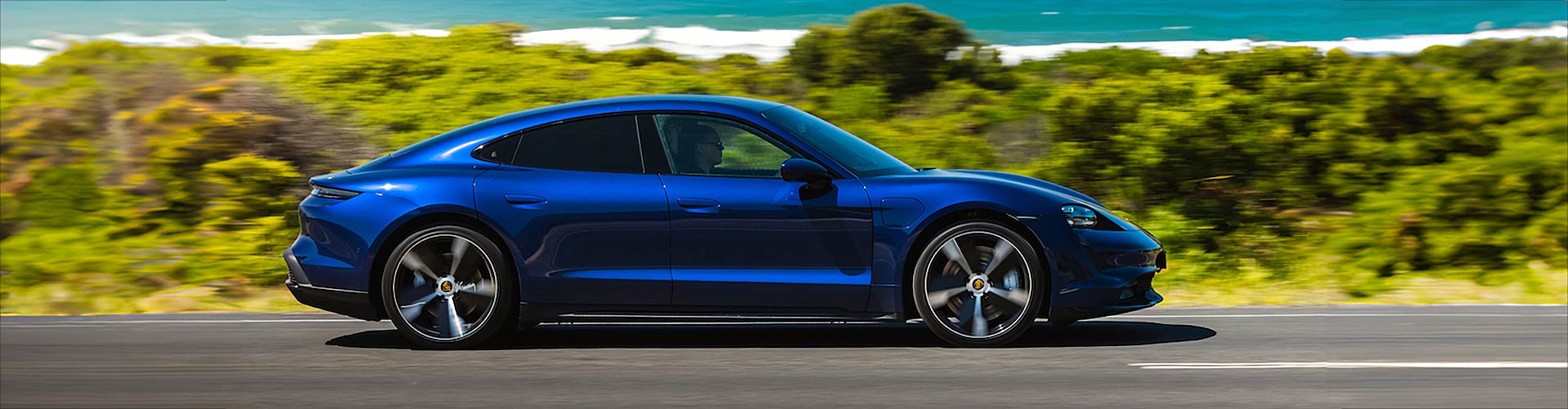 Blue 2022 Porsche Taycan driving next to beach
