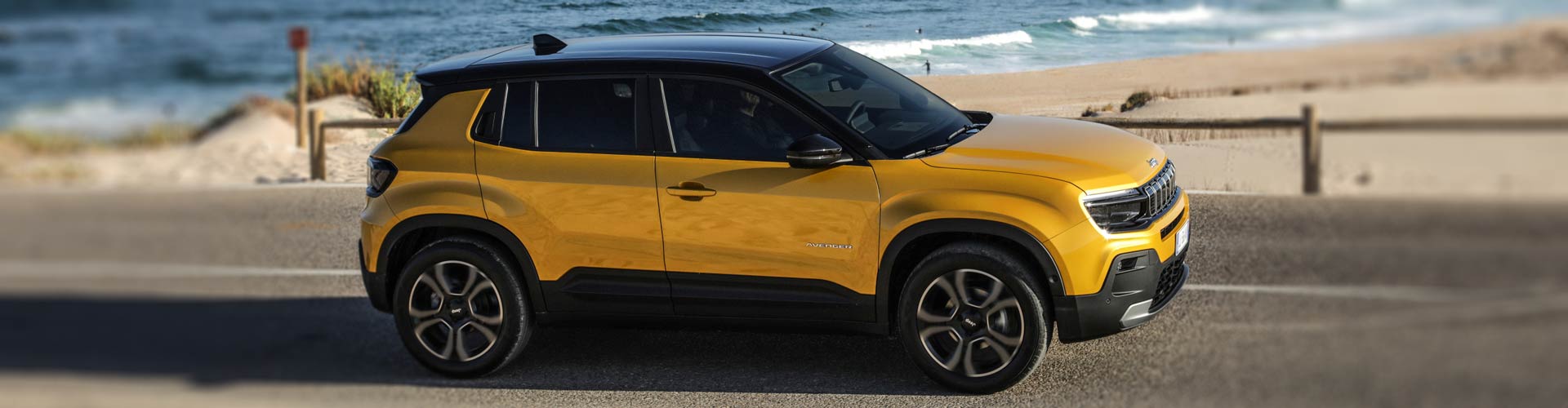 A yellow electric Jeep on a road by the beach