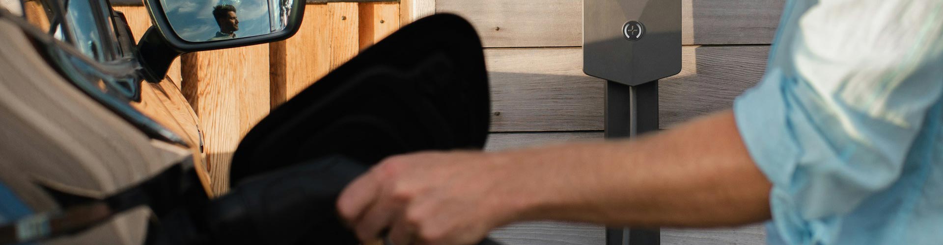 Man's hand charging EV out of focus in front of brick wall