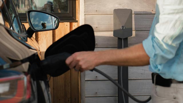Man's hand charging EV out of focus in front of brick wall