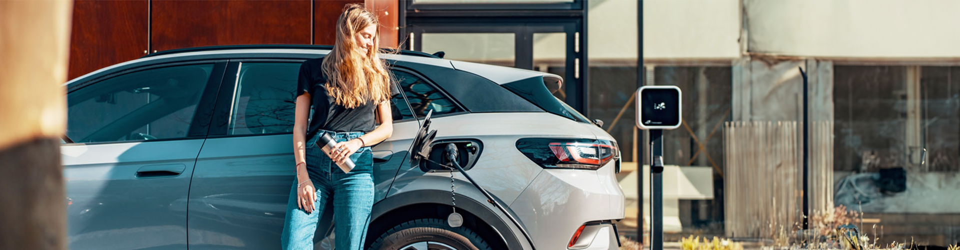 A woman leaning up against her car as it charges electrically  A woman leaning up against her car as it charges electrically