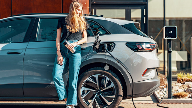 A woman leaning up against her car as it charges electrically A woman leaning up against her car as it charges electrically