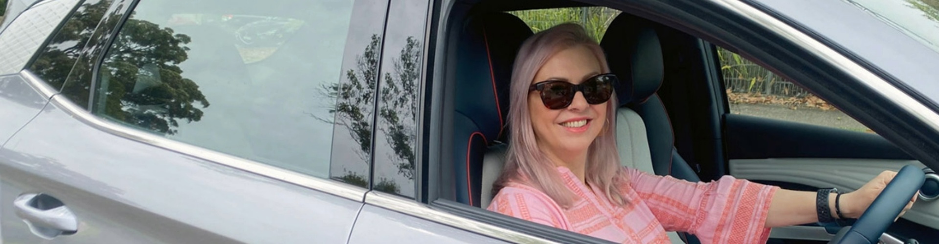 Side view of a lady sitting in the driver's seat of a car, looking to the side and smiling.