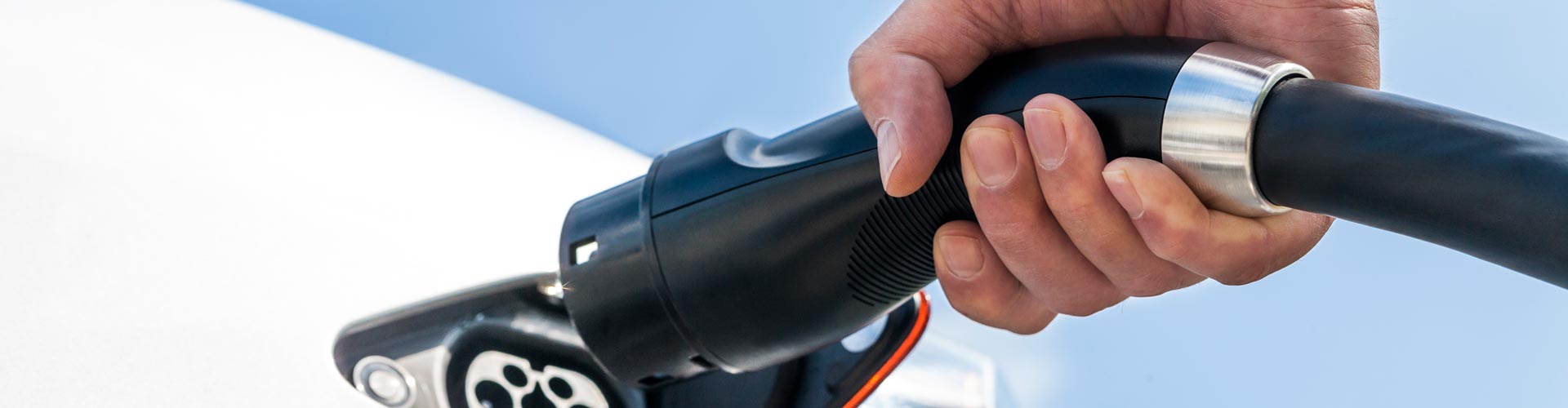 A hand puts a charging cable into an EV port