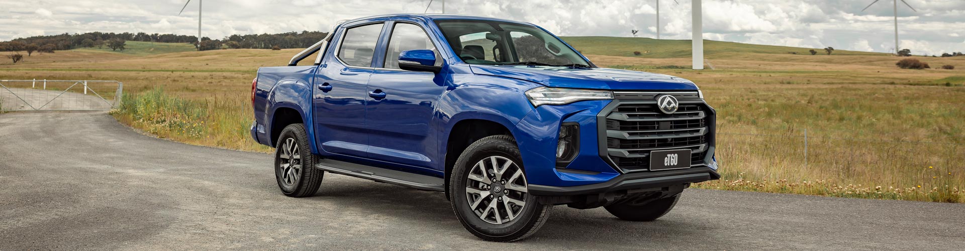 A blue LDV eT60 electric ute parked in front of a wind farm