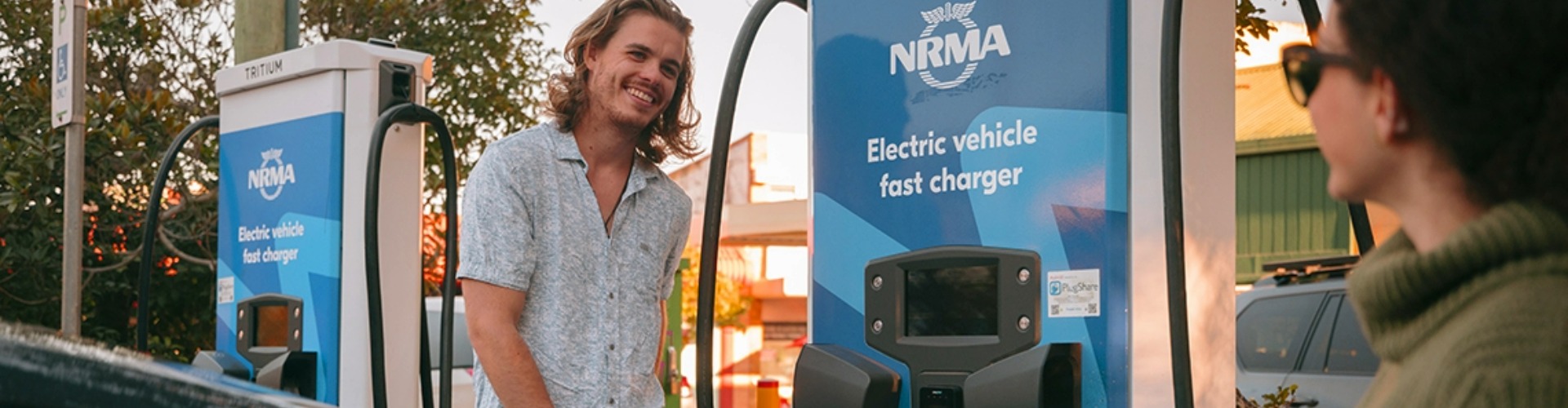 Man smiling at a women, while using an NRMA charging port to charge his electric vehicle.