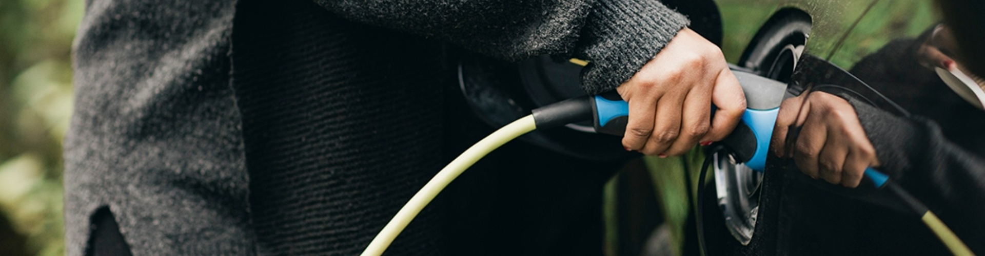 Side view of a hand holding an EV charger in a car charging port.