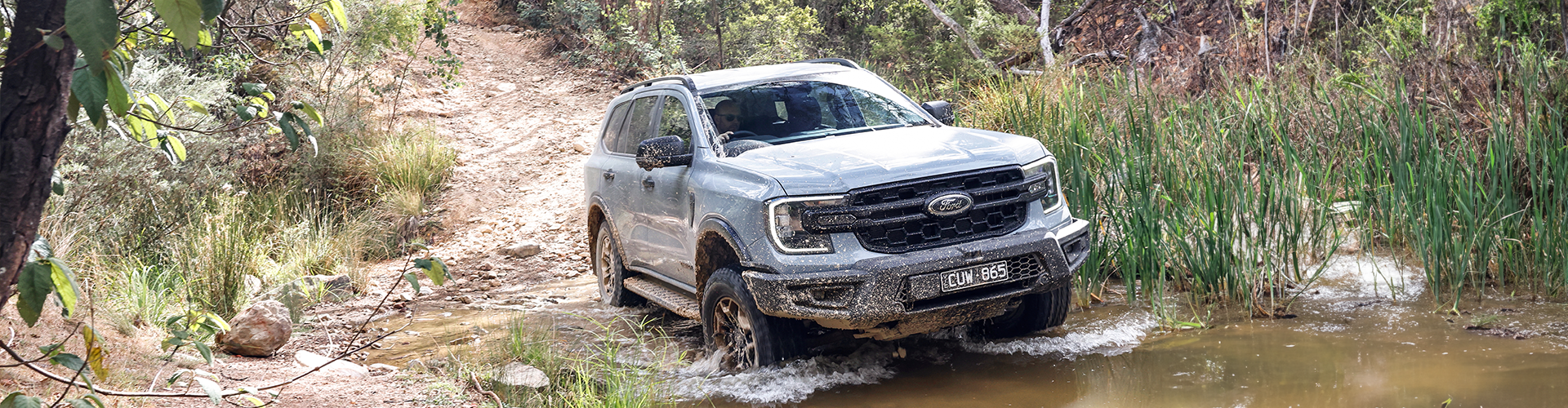 a grey SUV truck driving though a shallow creek in the bush