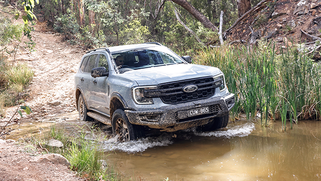 a grey SUV truck driving though a shallow creek in the bush