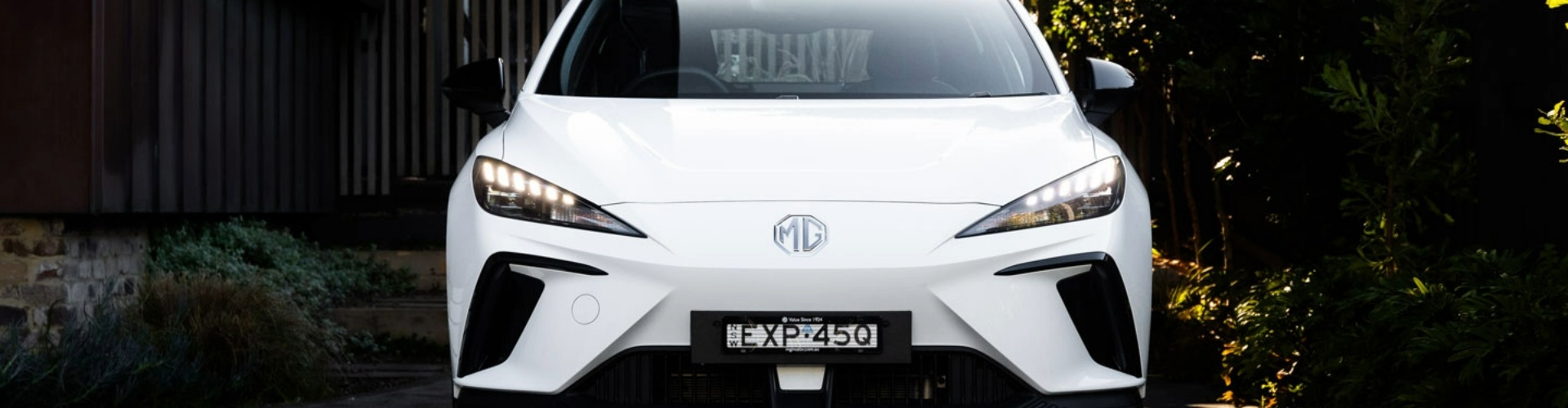 Front view of a white MG4 car parked in a dimly lit driveway.
