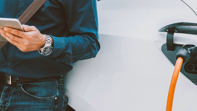 Someone reads their tablet while waiting beside their charging EV