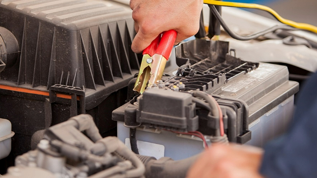 Close-up of a red jumper lead being applied to the positive post of a car battery