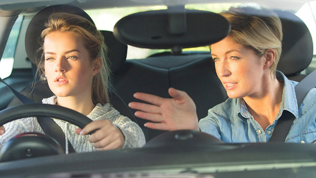 A young woman learning to drive beside her driving instructor