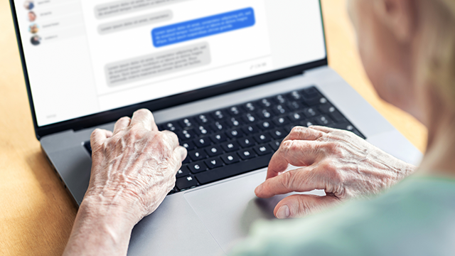 An old woman's hand typing on a laptop keyboard into facebook messenger