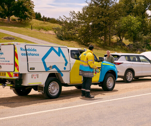 A roadside assistance worker in NRMA uniform prepares to help the driver of a white SUV that has broken down on a road.