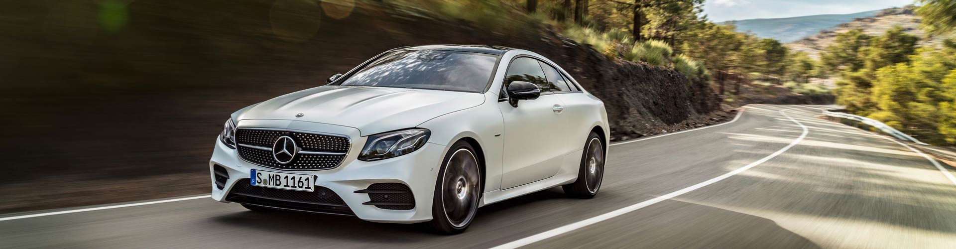 White Mercedes-Benz E-Class driving fast on a road surrounded by trees