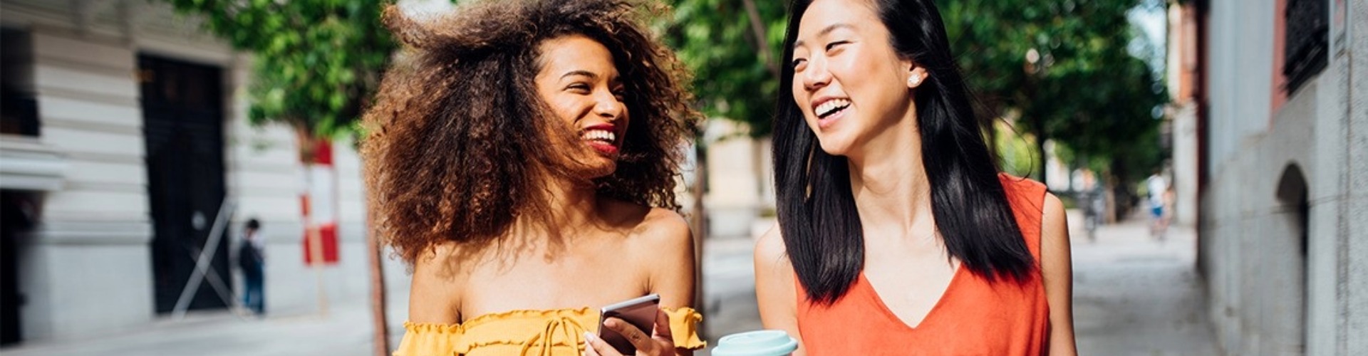 A pair of friends walk down the street together laughing