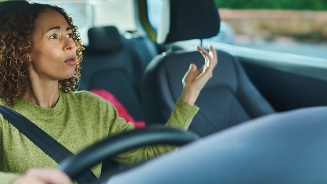 A seemingly frustrated driver looks into her rearview mirror making hand gestures