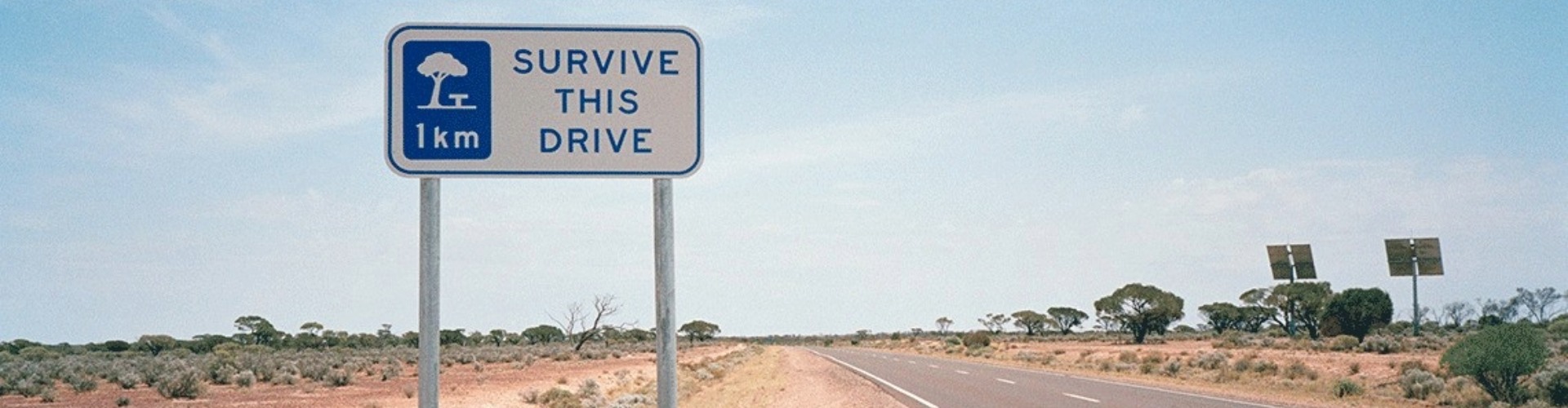 A sign on a country road saying 'Survive this drive'