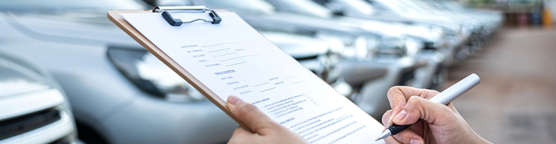 Someone goes through a checklist on a clipboard, while looking at a row of cars