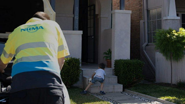 NRMA technician working under a car bonnet in the driveway of a family home