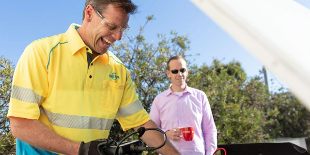 NRMA technician looks under a car bonnet while a driver looks on