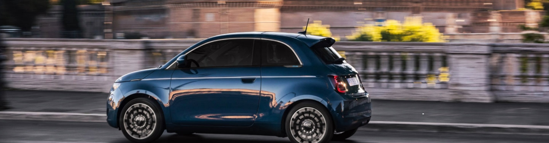 Side view of a blue Fiat 500 driving along a road.