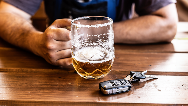 A near-empty glass of beer on a counter, with the drinker's forearms and keys visible