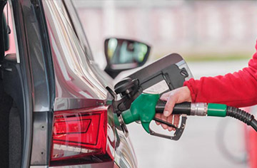 Arm in red sleeve putting fuel in a car seen from rear of car