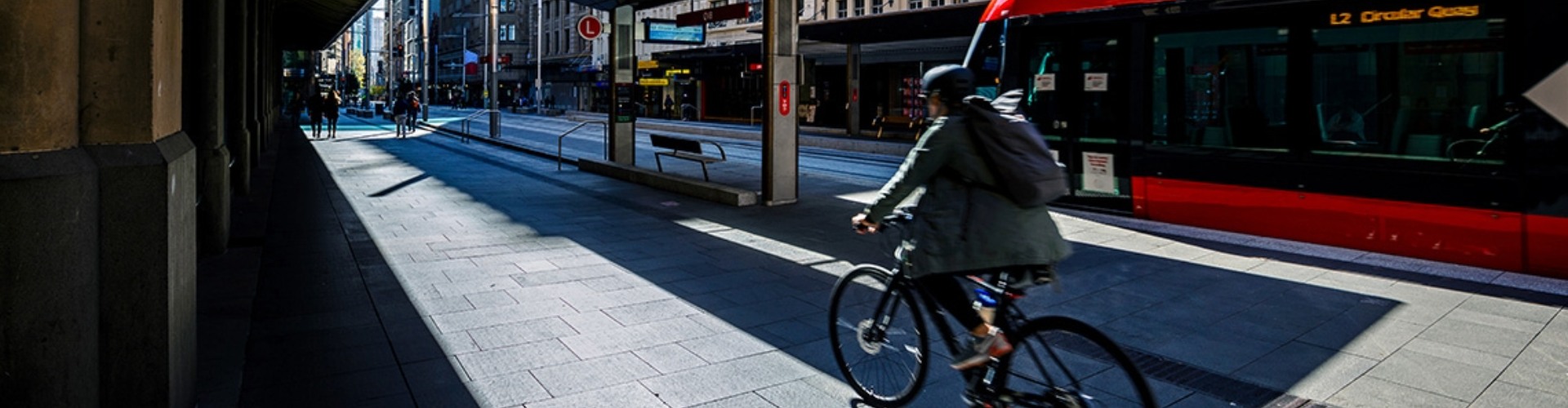 A cyclist rides beside a light-rail along a CBD thoroughfare