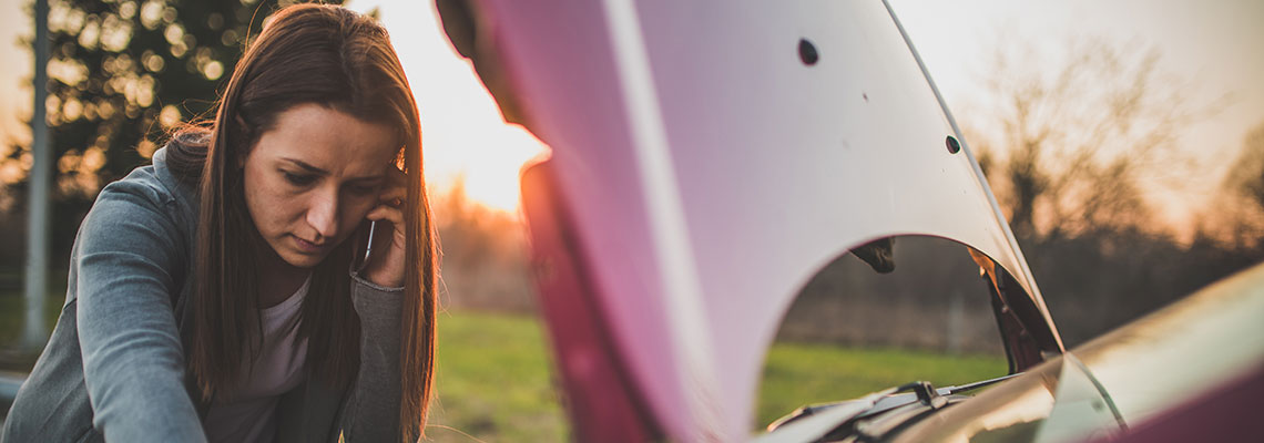 How do car warranties work ? A woman on the phone looking into car engine at dusk