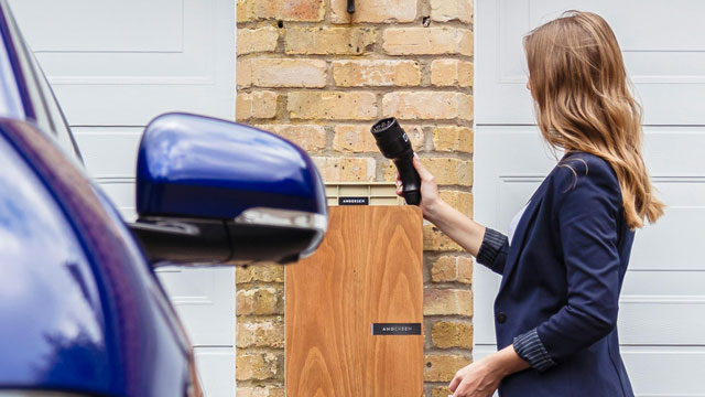 woman-using-ev-charger-at-home-640x360 Woman charging an EV in front of a garage