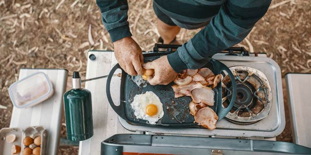 Downward view of a person cooking eggs and bacon on a portable bbq