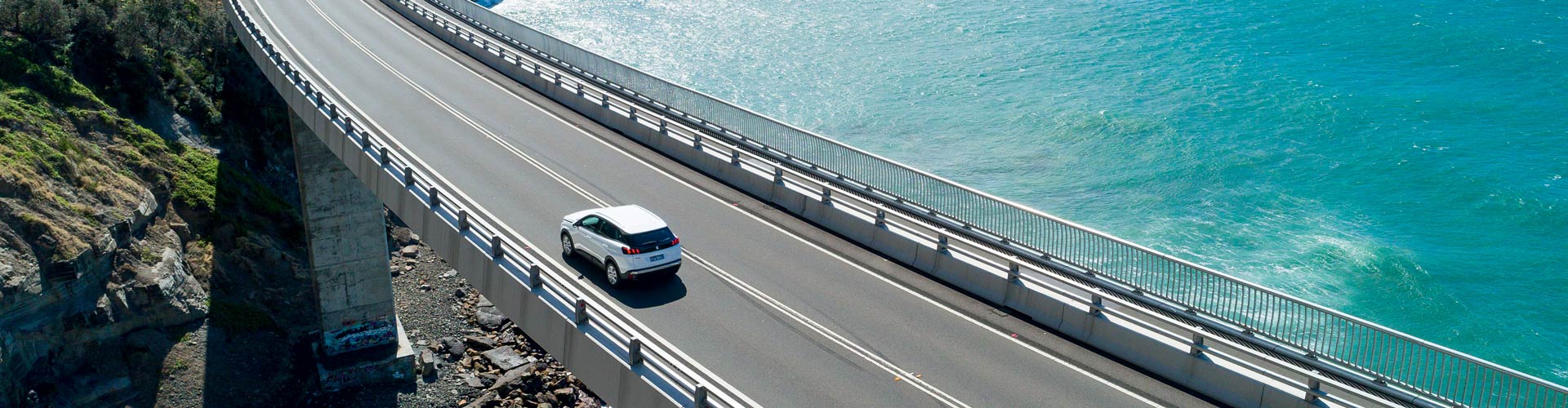 A car drives on Seacliff Bridge above aqua ocean