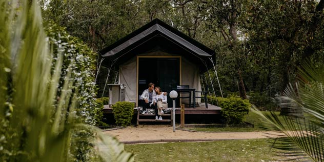 A young couple relaxing on the balcony of a glamping tent at the NRMA Ocean Beach Holiday Resort