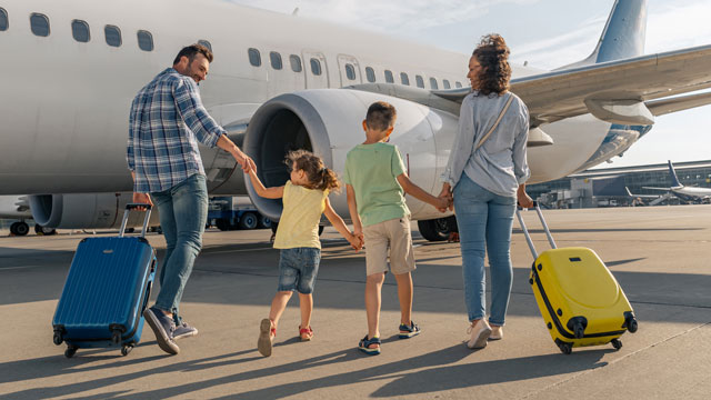 Family of four boarding a plane with yellow and blue carry on bags