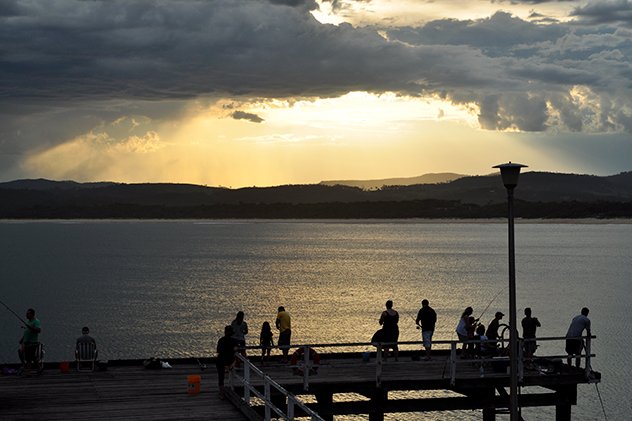 People fishing on a pier during a golden sunset
