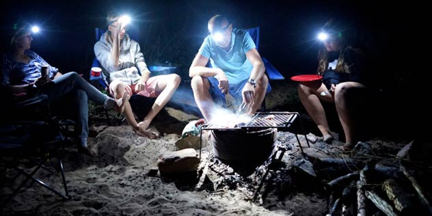 A family sits around a campfire with head torches on