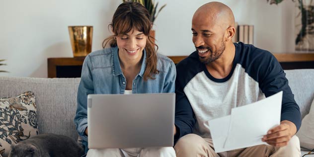 A woman and man plan a trip at the laptop on a couch