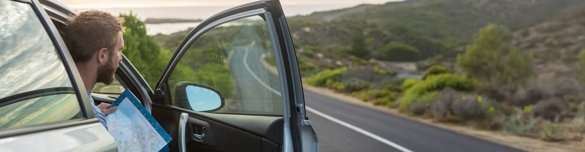 Man holding a map in the a car by the side of the road
