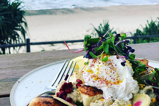 A foodie plated poached egg on a plate with the beach behind at Shelly Beach cafe, Ballina
