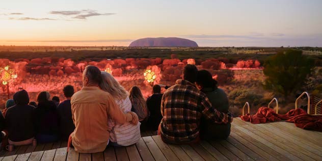 Friends sit looking at Uluru at sunset