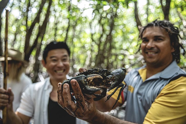 Indigenous man holds crab next to tourist