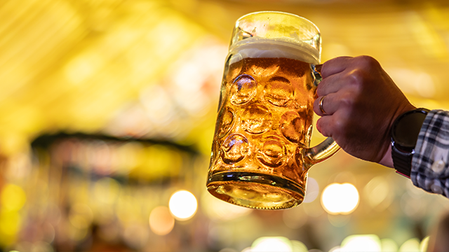 a hand in a blue check shirt holding a pint of beer