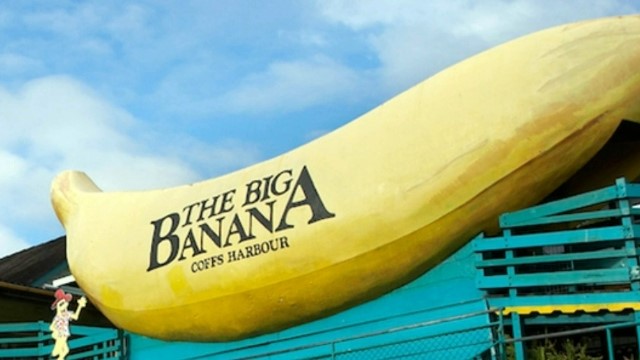 big-banana-nsw-640x360 A giant yellow banana sculpture with the words The Big Banana, Coffs Harbour, written in black along the side, in front of a clubhouse and palm trees.